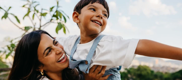 A boy smiling with his mother as she picks him up