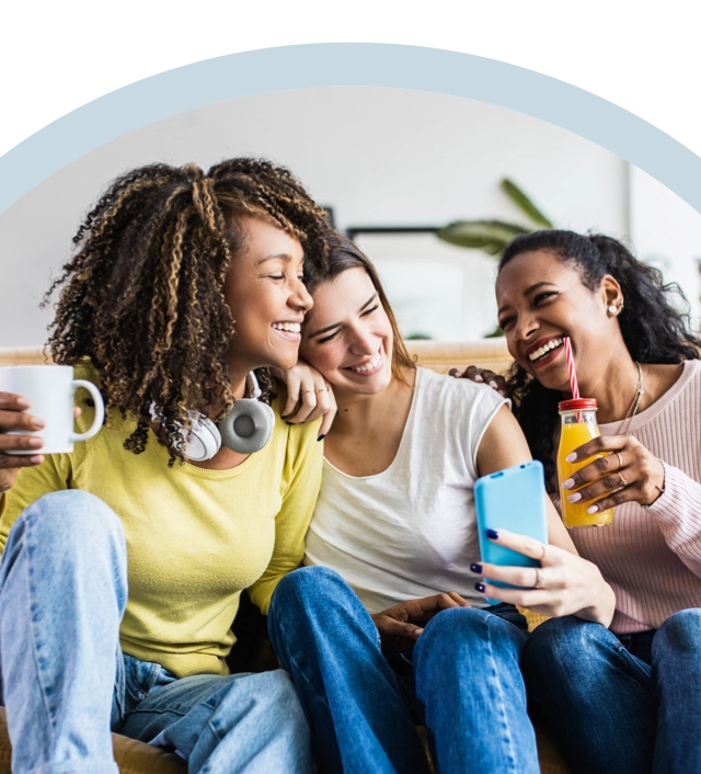 Three friends smiling, looking at a phone and enjoying beverages, with happy, confident smiles, with Spirit Dental coverage.